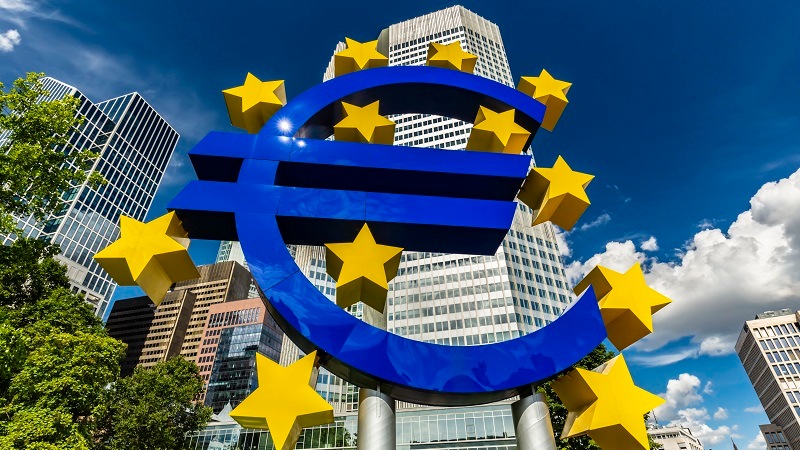 A statue depicting the euro currency symbol in front of tower blocks in Frankfurt.